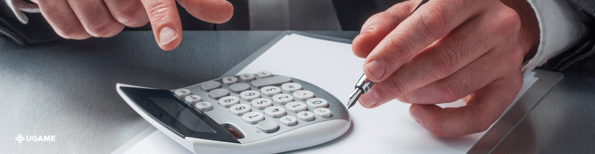 Mãos de um homem apoiadas em uma mesa com uma prancheta e uma calculadora em cima. A mão esquerda segura uma caneta